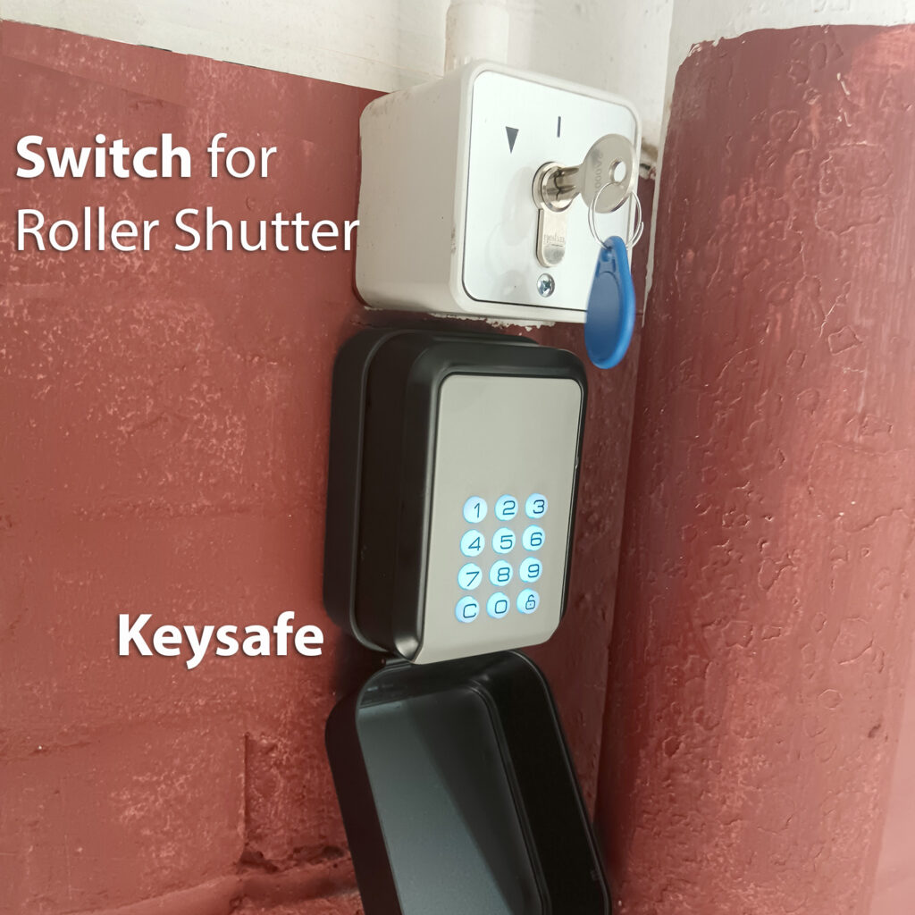 keysafe - Birmingham SelfStorage Lockbox with keys and a keypad keypad-style key safe mounted on a red brick wall; blue key tag hanging from the white box below a switch plate.