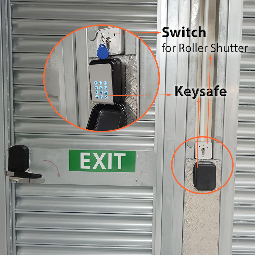 Lockbox with keys and a keypad keypad-style key safe mounted on a red brick wall; blue key tag hanging from the white box below a switch plate.